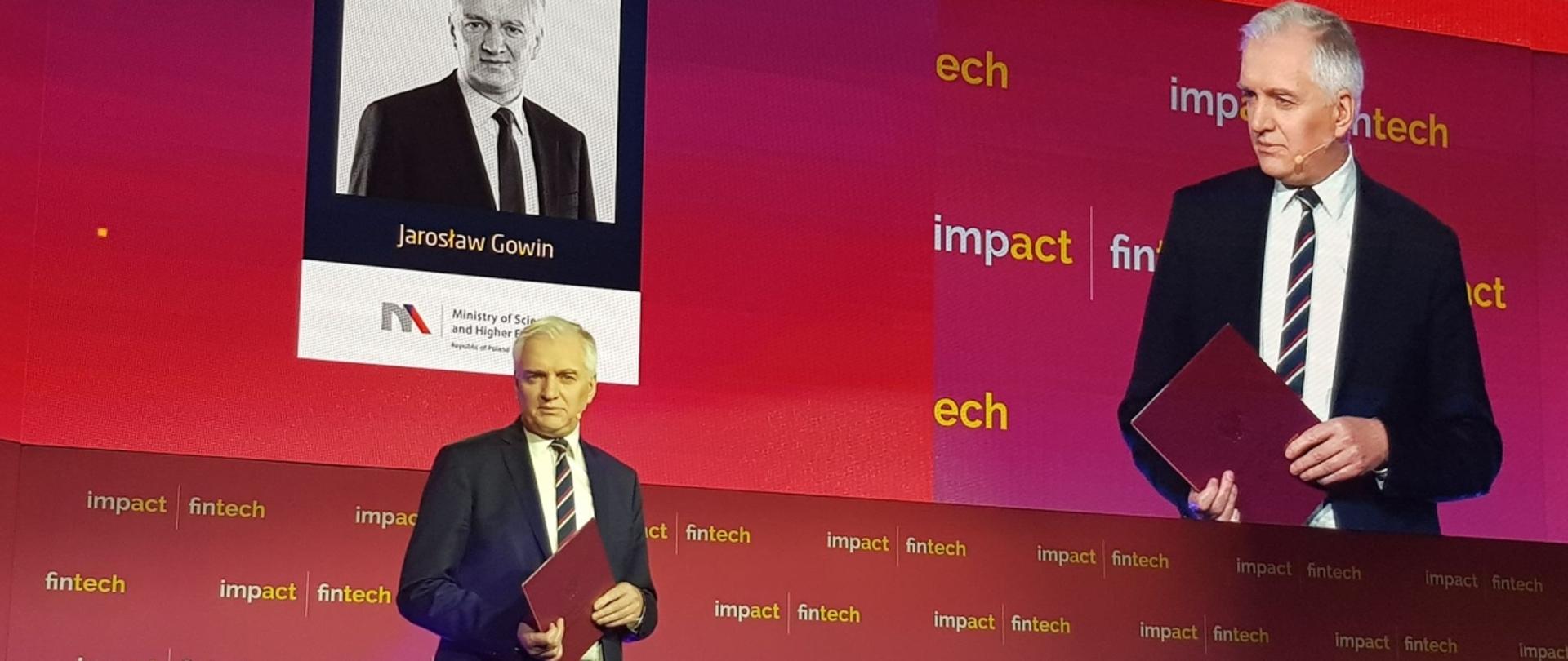 Minister Gowin przemawia stojąc na tle czerwonej ściany z napisem Impact fintech’19