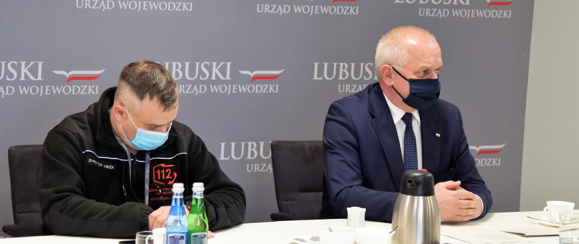 Wojewoda z dyrektorem BZK siedzą przy stole prezydialnym, za nimi ścianka promocyjna urzedu