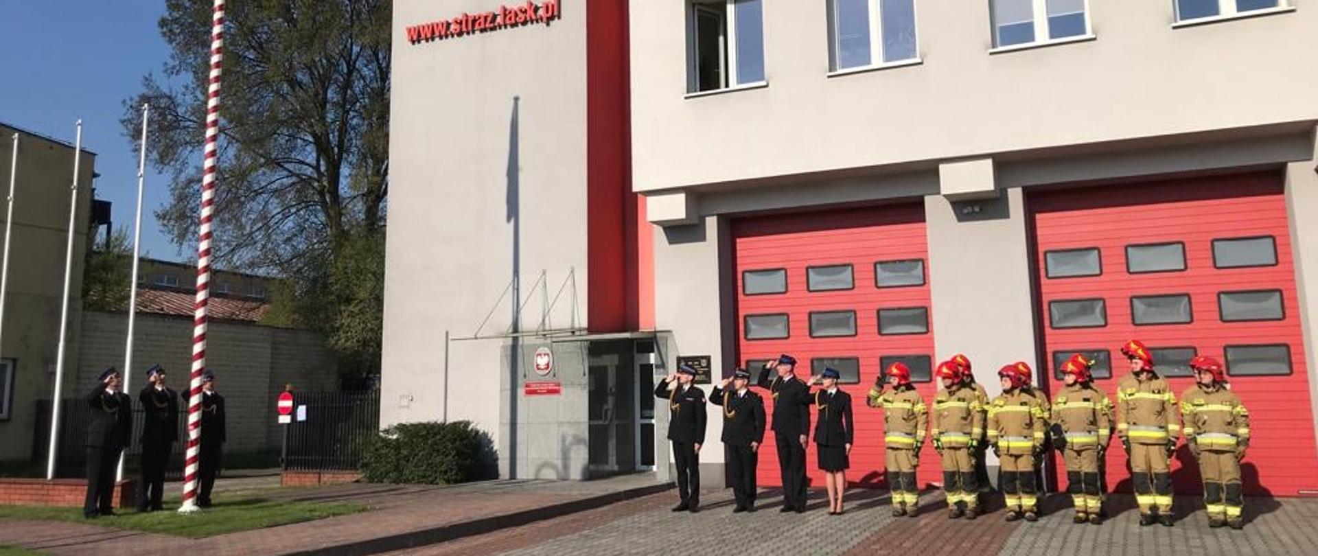 Zdjęcie przedstawia strażaków PSP podczas uroczystego wciągnięcia na maszt flagi państwowej z okazji Dnia Flagi Rzeczypospolitej Polskiej