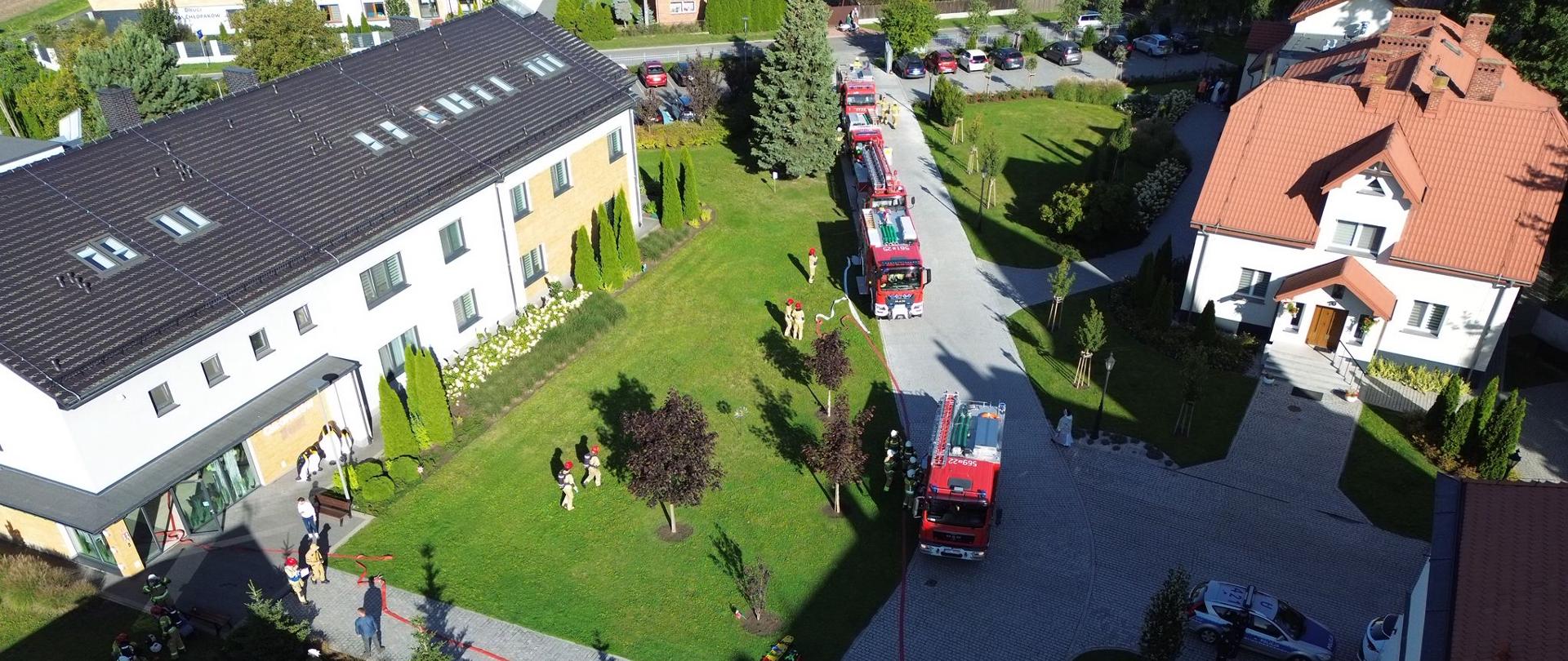 widok z góry na teren zielony i budynek z samochodami strażackimi