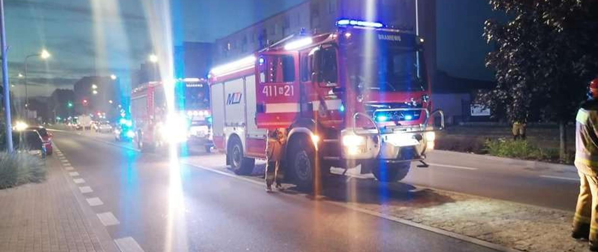 Zdjęcie zrobione nocą. Na zdjęciu dwa swa samochody strażackie na światłach drogowych i niebieskich ostrzegawczych.