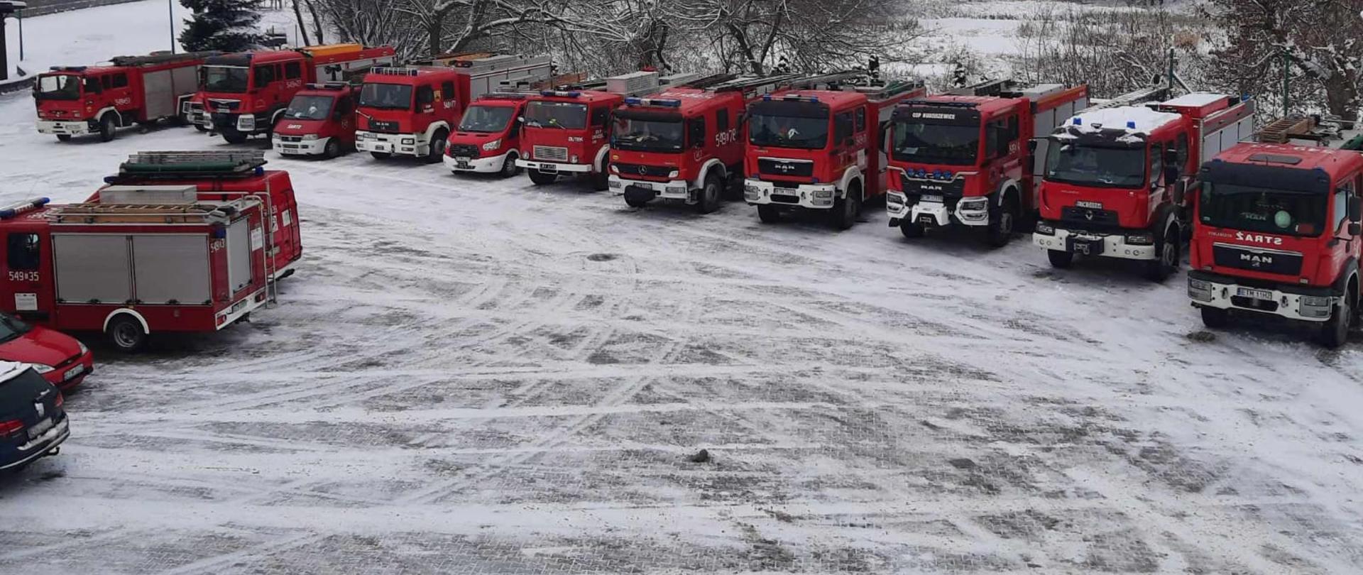 Zdjęcie przedstawia pojazdy pożarnicze stojące na placu przed Komendą PSP w Tomaszowie Mazowieckim. Plac Komendy pokryty jest śniegiem. Zdjęcie wykonane z wysokości.