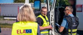 Funkcjonariusze litewskich służb kontrolnych pobierają dokumenty od kierowcy ciężarówki.
