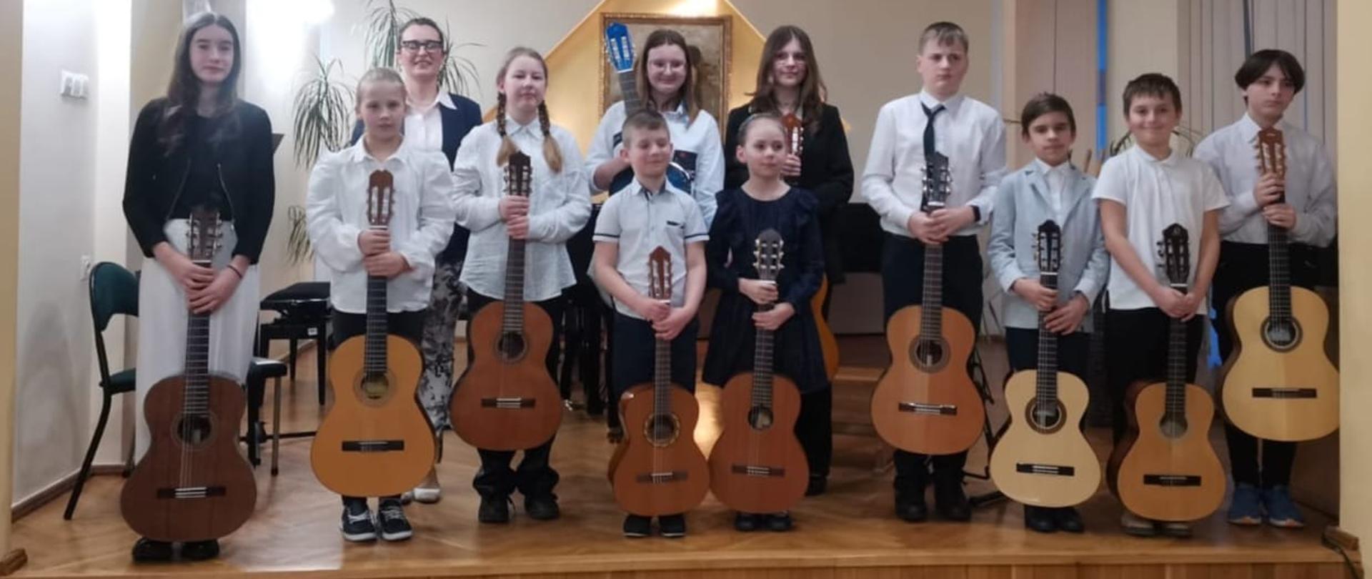 Galeria 18 zdjęć z Wiosennego Koncertu Gitarowego uczniów klas gitary A. Kozakowskiej i W. Kozakowskiego - 22 marca 2024. Uczestnicy konkursu grają na gitarze na scenie auli PSM w Kłodzku