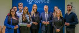 Pod niebieską ścianką z napisem Uniwersytet Szczeciński stoi grupa ludzi, pośrodku minister Wieczorek.