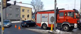 Na fotografii znajduje się samochód pożarniczy, za nim uszkodzony samochód osobowy oraz patrol Policji