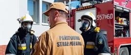 Egzaminator z PSP stoi tyłem, za nim dwaj strażacy OSP w sprzęcie OUO.