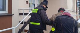 Strażak z inną osobą pomaga wejść po schodach starszej kobiecie. Schody prowadzą do punktu szczepień.