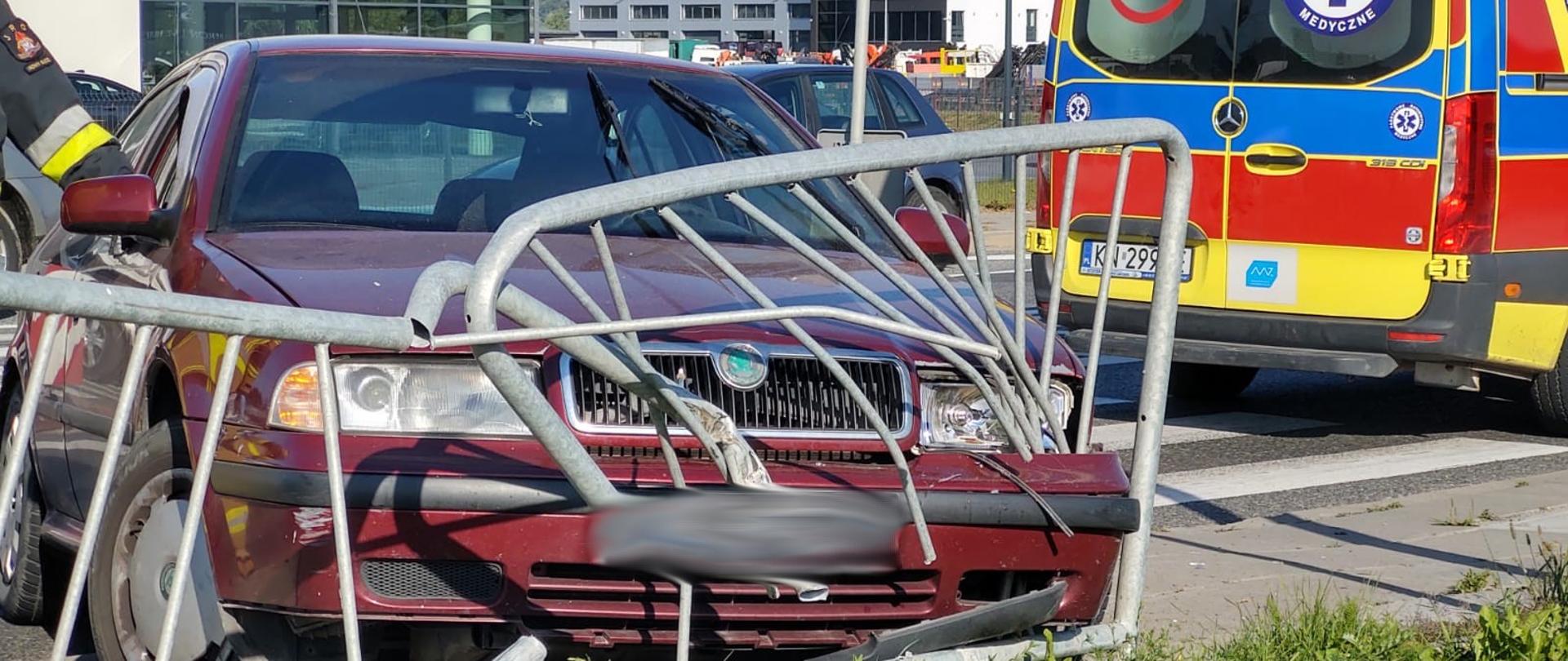 Samochód i barierki w które uderzył przodem. Obok karetka Pogotowia ratunkowego 