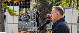 Mężczyzna prezydent Polski przemawia przez mikrofon obok jest trumna z flagą Polski.