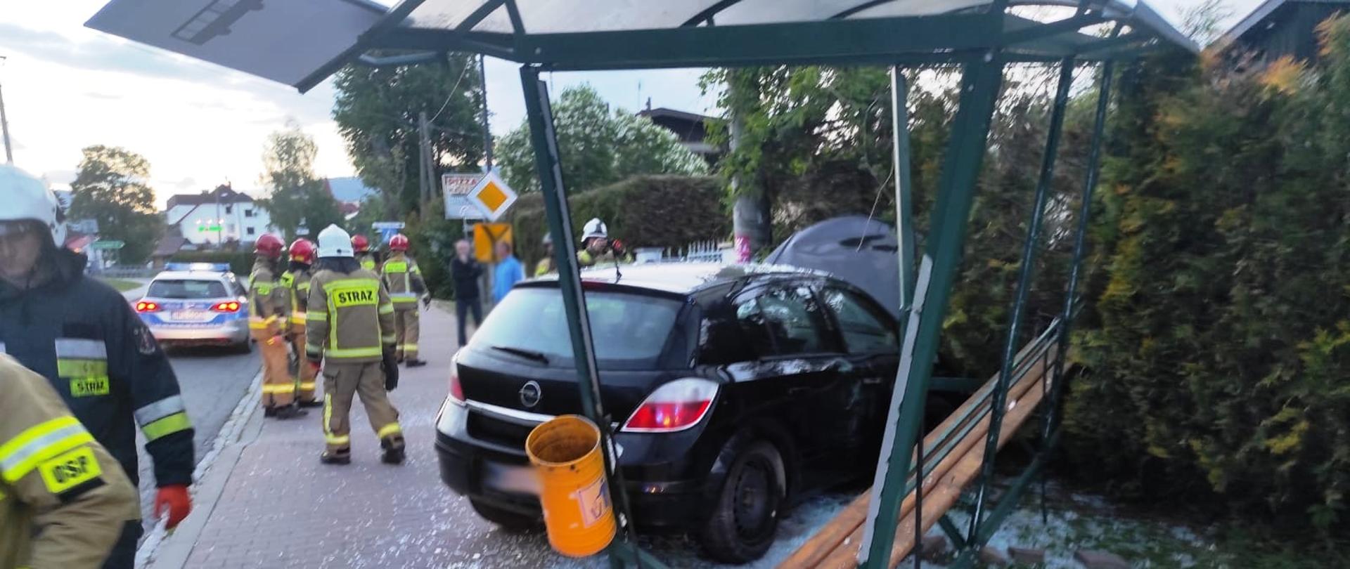 Widok od tyłu samochodu w przestrzeni przystankowej a obok strażacy.