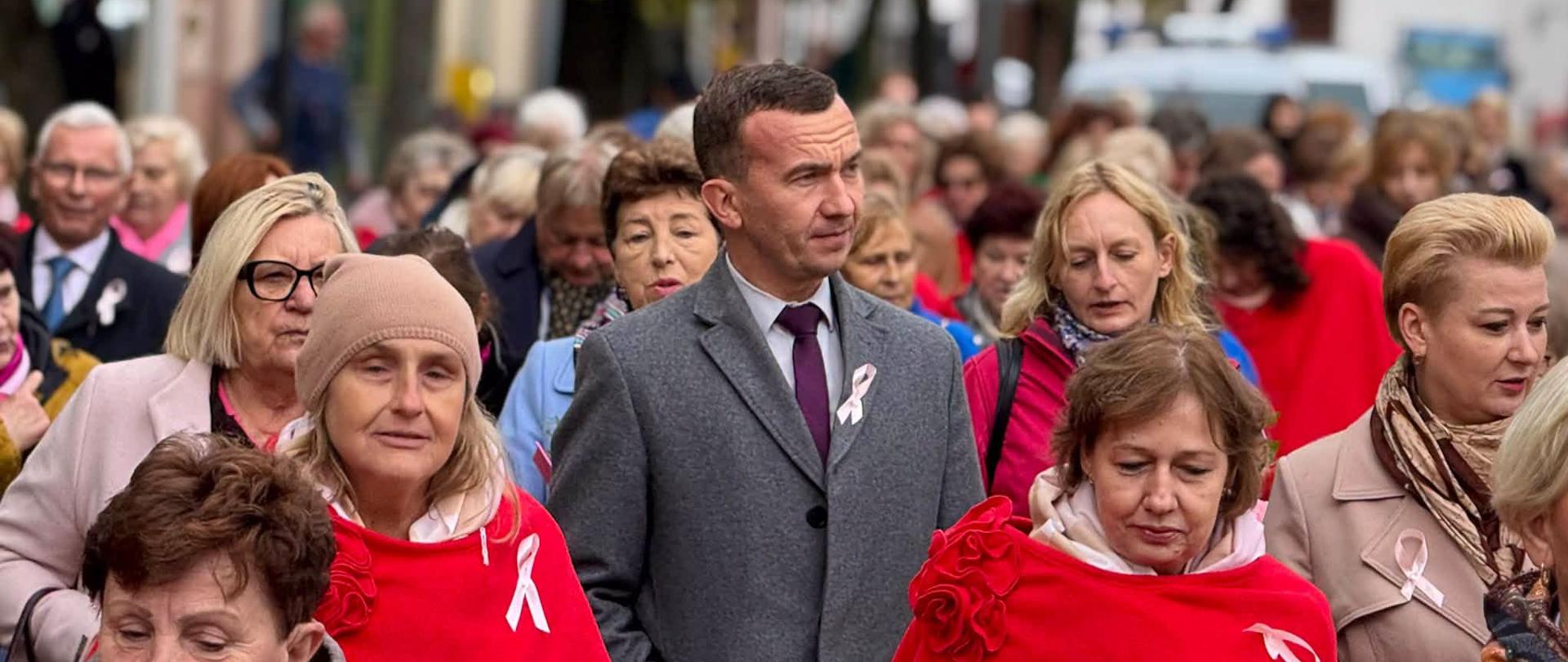 Wicewojewoda w szarym płaszczu uczestniczy w przemarszu, idąc wspólnie z pozostałymi uczestnikami wydarzenia.