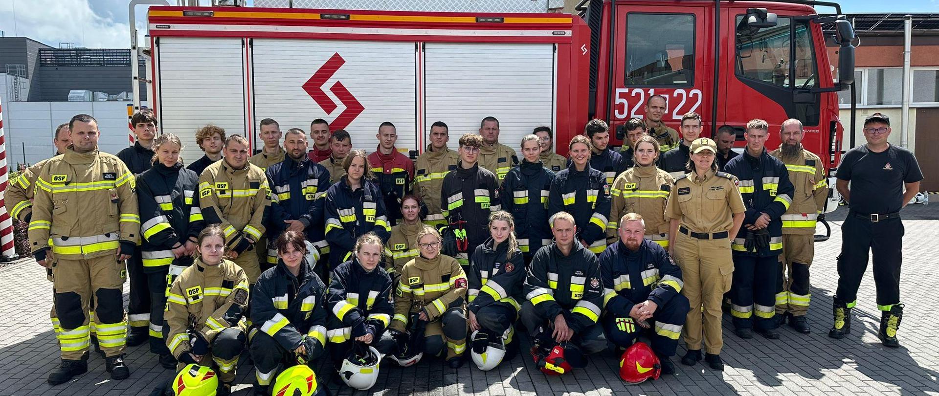 Pamiątkowe zdjęcie uczestników szkolenia, w tle samochód pożarniczy.