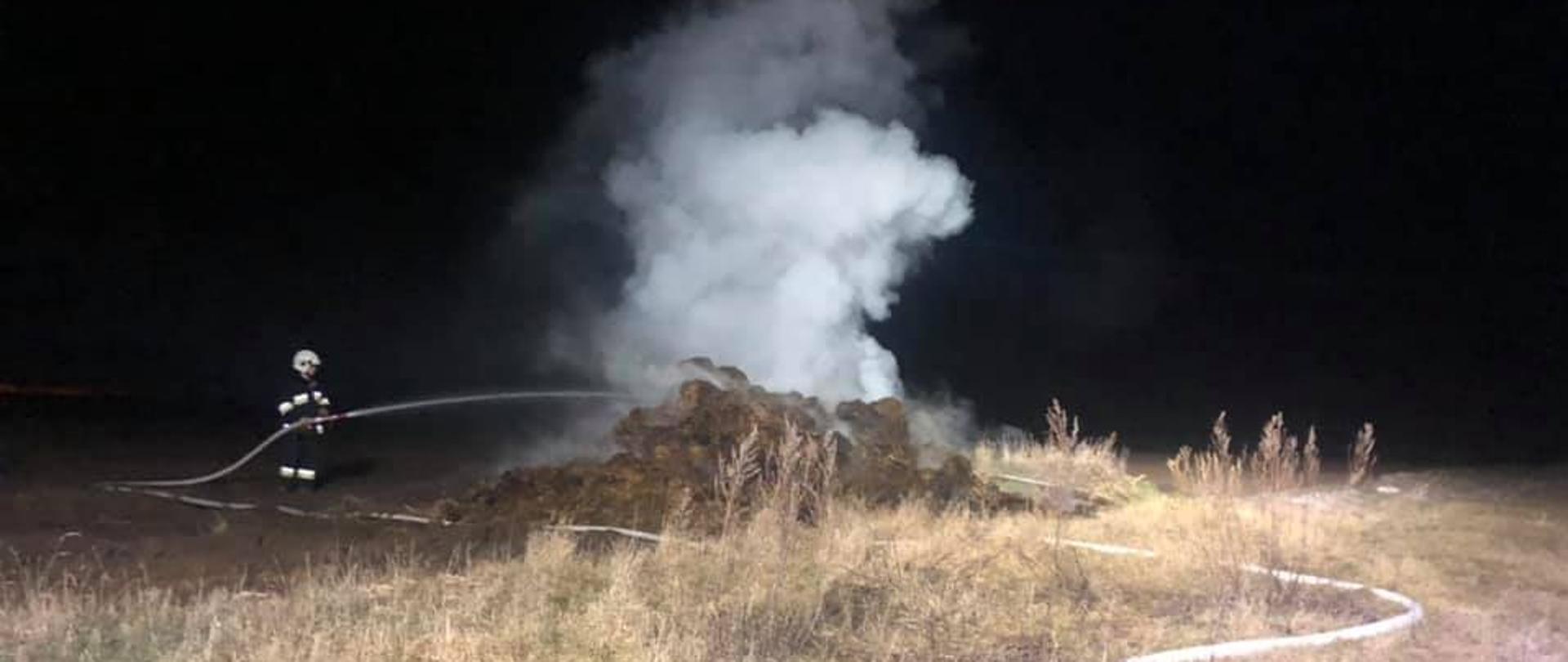 Noc, sterta na polu, dym, strażak gasi.