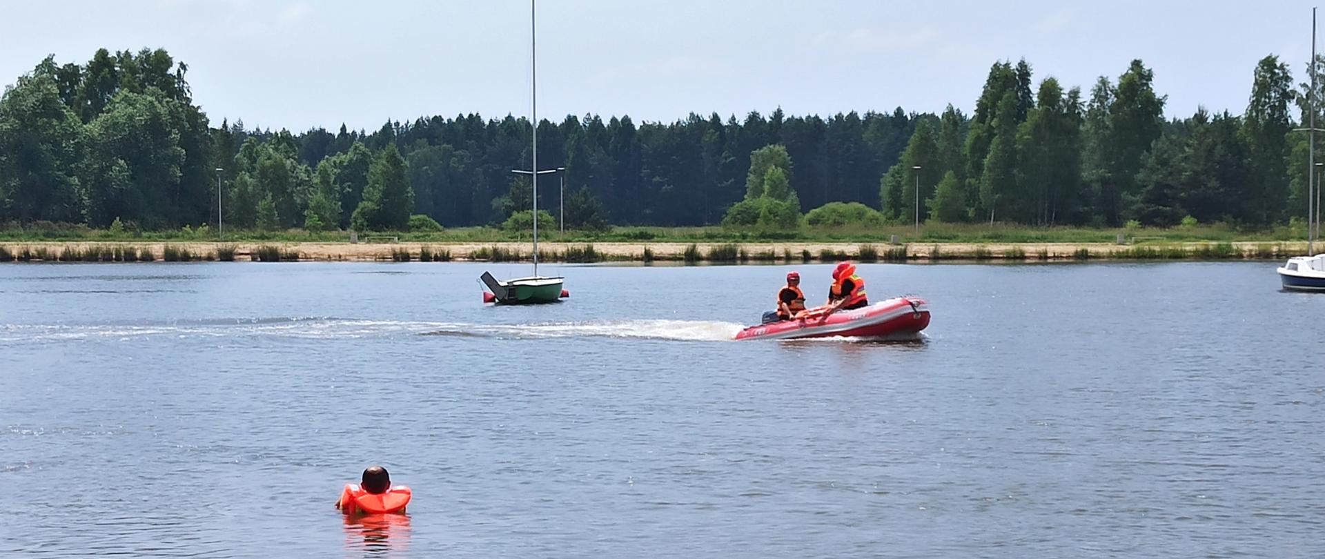 strażacy na łodzi ratowniczej podpływają do osoby będącej w wodzie