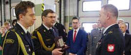 Komendant i zastępca komendanta powiatowego wręczają pamiątkowy prezent strażakowi przechodzącemu w stan pozasłużbowy.
