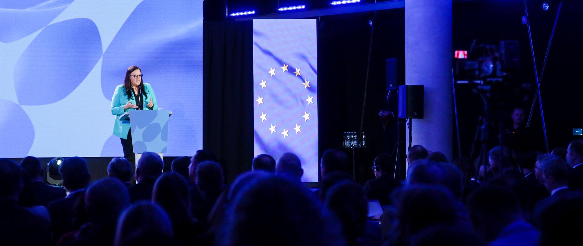 W sali konferencyjnej wiceminister Małgorzata Jarosińska-Jedynak na scenie przed mikrofonem. Przed nią publiczność.