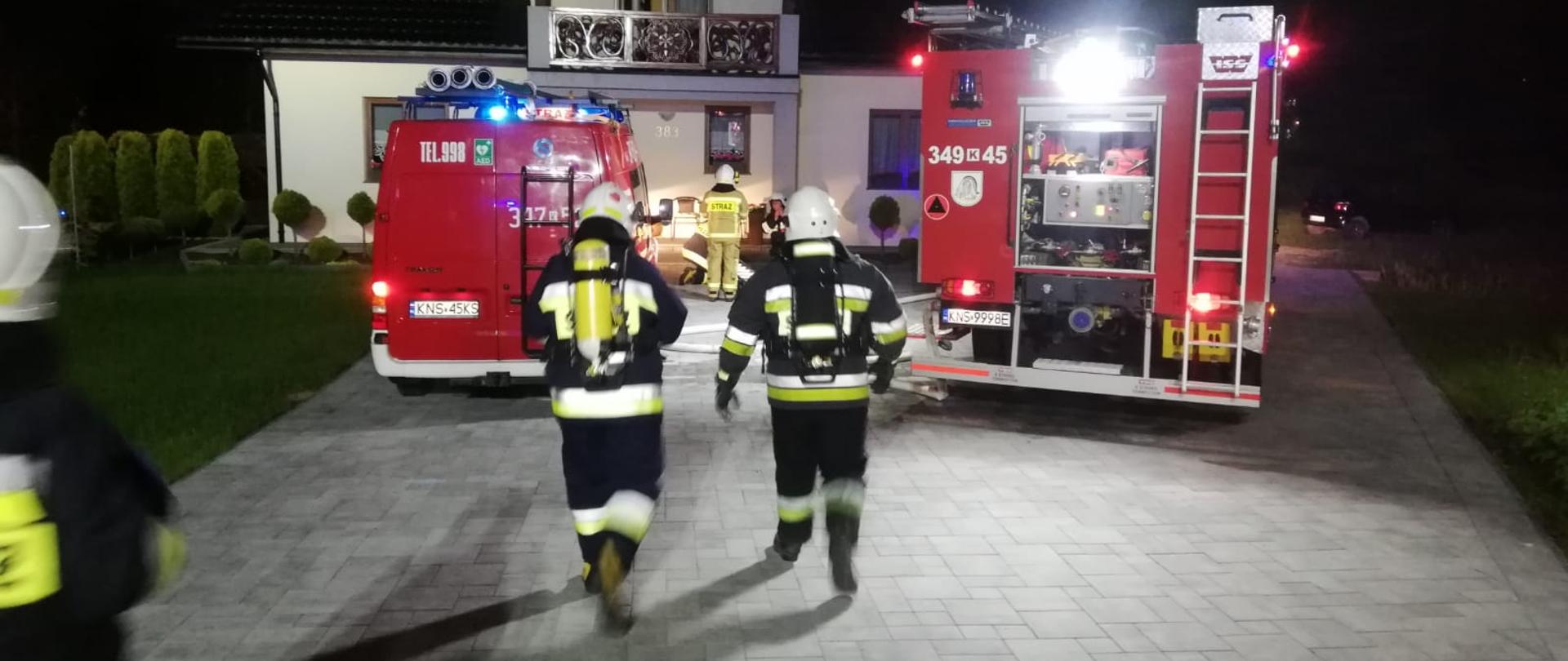 Strażacy i samochody pożarnicze. W tle budynek w którym prowadzono działania ratownicze.