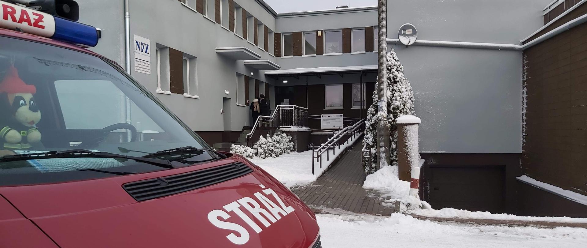 Strażak pomaga osobie starszej wsiąść do strażackiego samochodu. 