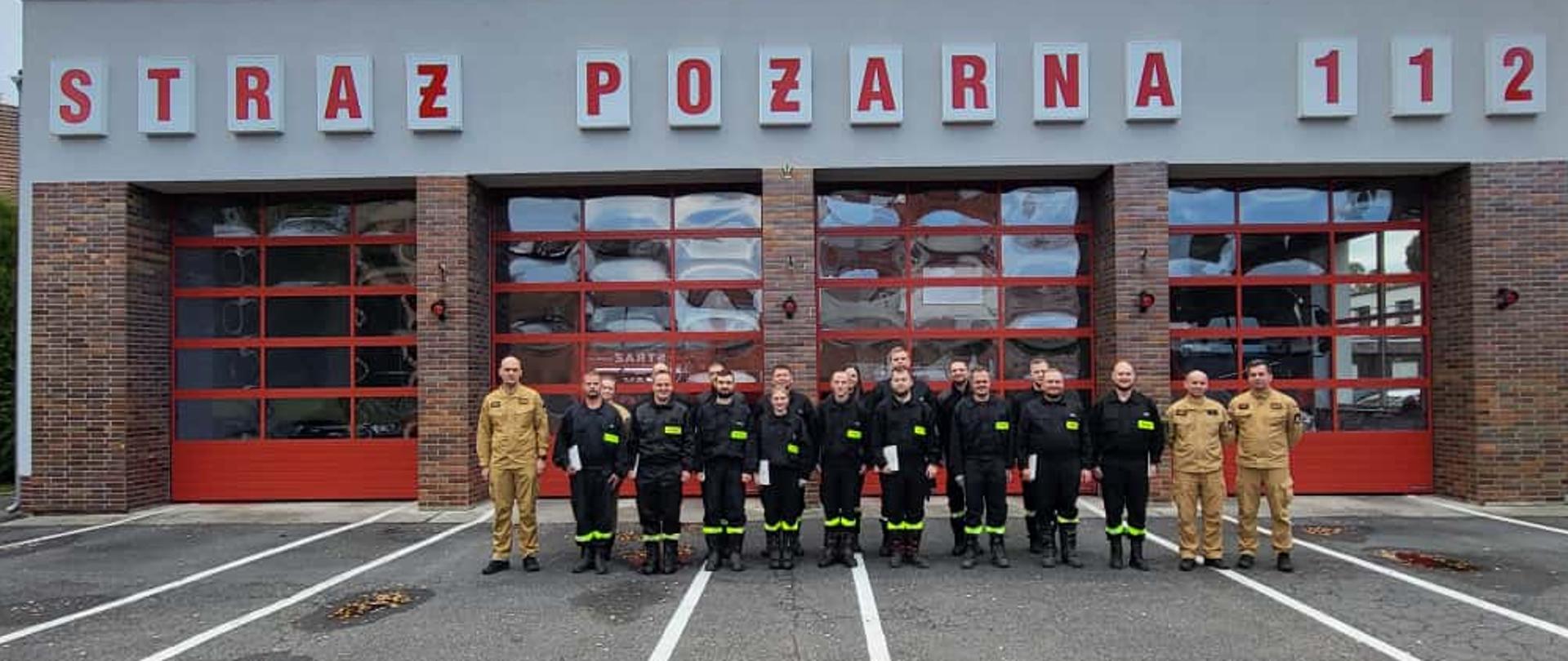 Uczestnicy szkolenia kierującego działaniem ratowniczym dla strażaków ratowników Ochotniczych Straży Pożarnych podczas podsumowania zajęć przed budynkiem Państwowej Straży Pożarnej, z zaświadczeniami uprawniającymi do pełnienia zadań dowódcy.