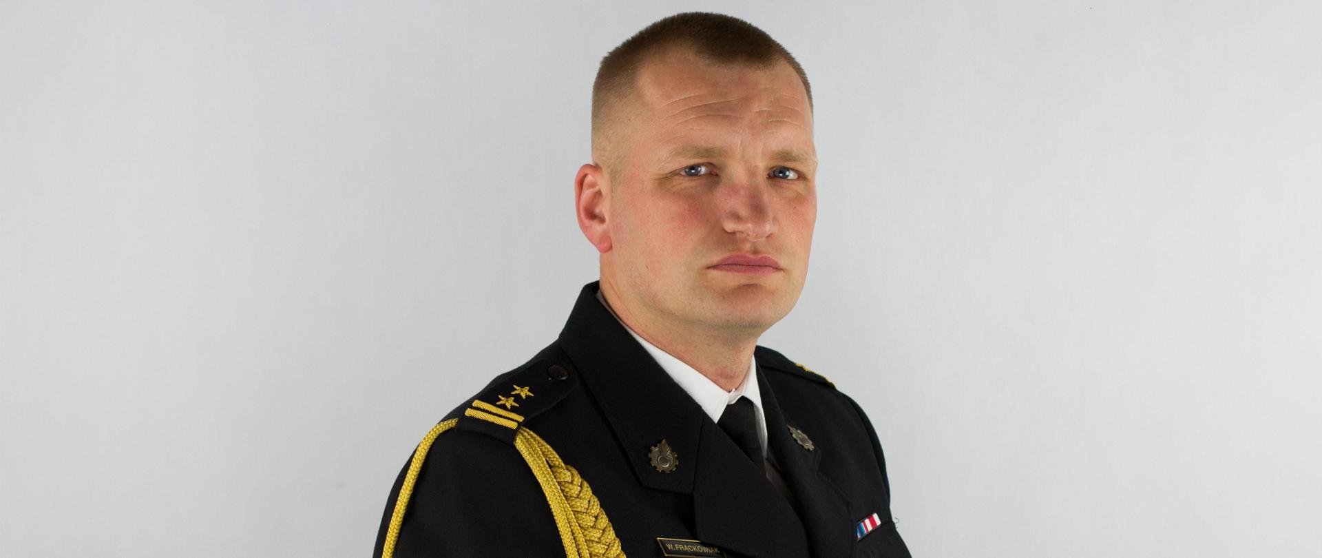 Mężczyzna w mundurze na białym tle, mundur czarny, po lewej stronie znajduje się sznur galowy zwisający od ramienia