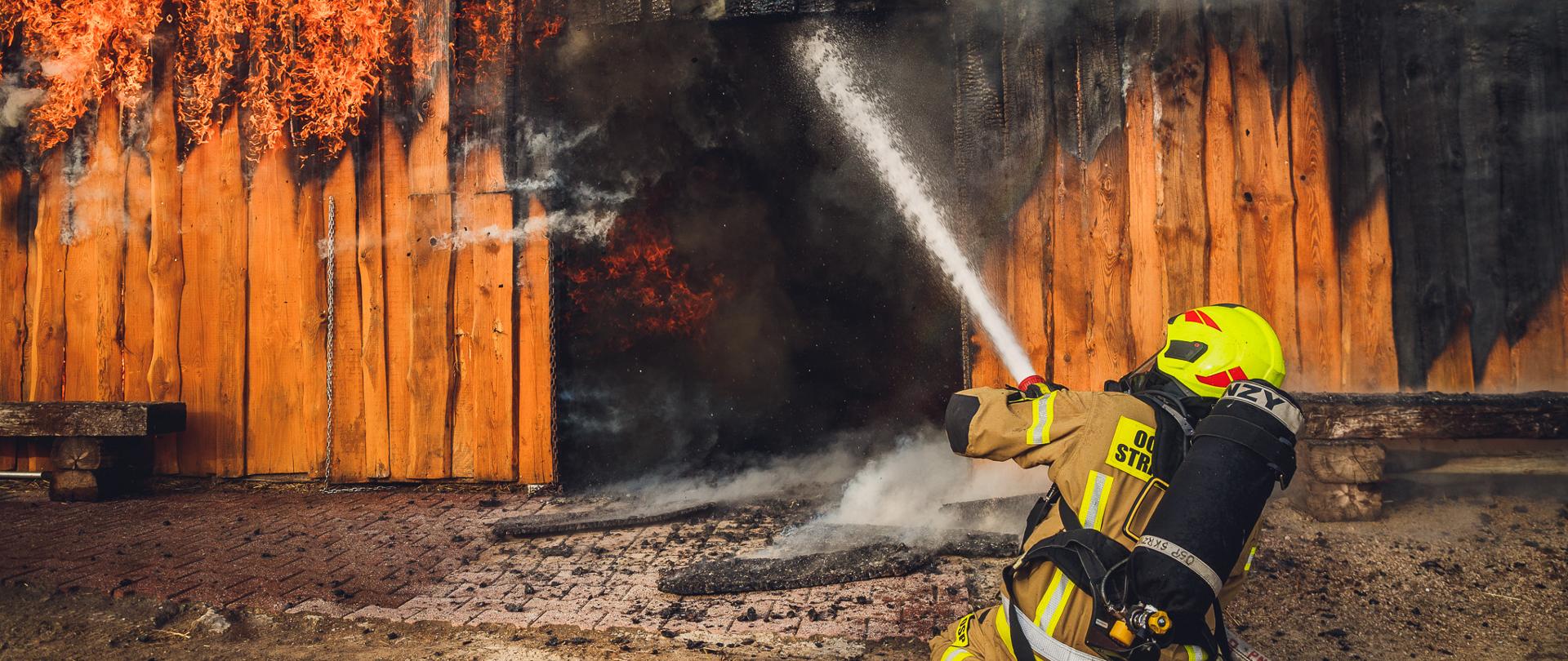 Strażak klęczący na ziemi podający strumień wody na palący się obiekt