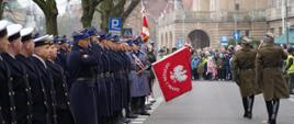Przegląd wojsk i funkcjonariuszy. Od lewej końcówka formacji marynarki wojennej, następnie państwowa straż pożarna, a następnie widoczne sztandary policji itd. W tle cywile oraz widok na budynek Muzeum Narodowego oraz Akademii Morskiej