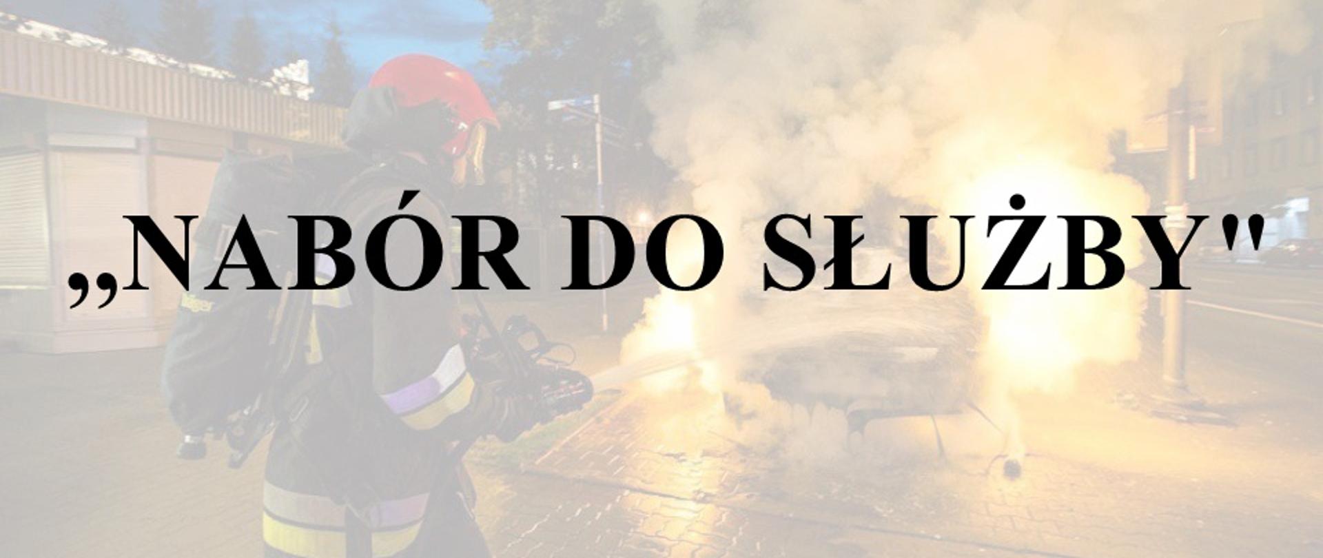 Na zdjęciu znajduje się napis informacyjny o treści ,,Nabór do służby" który organizowany jest w KP PSP Grójec. W tle widoczna jest akcja gaśnicza jednego ze strażaków. 