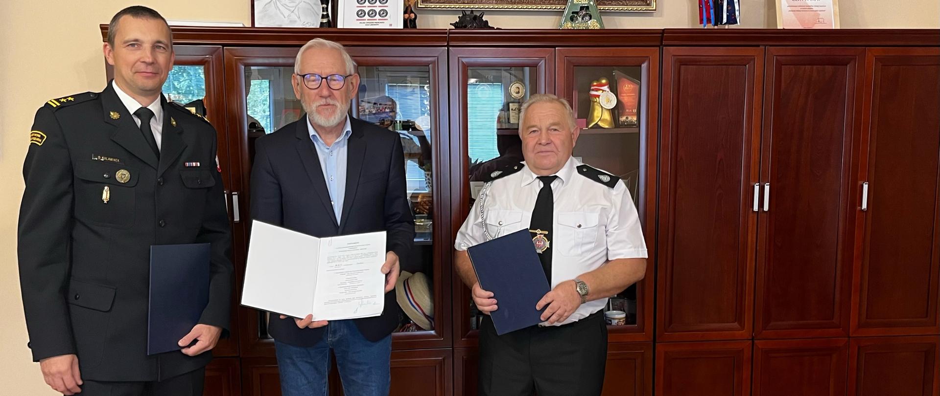 Zdjęcie przedstawia trzech mężczyzn trzymających teczki z dokumentami. Na zdjęciu znajduje się Komendant Powiatowy PSP w Brzegu, Burmistrz Grodkowa i Prezes OSP Wierzbnik.