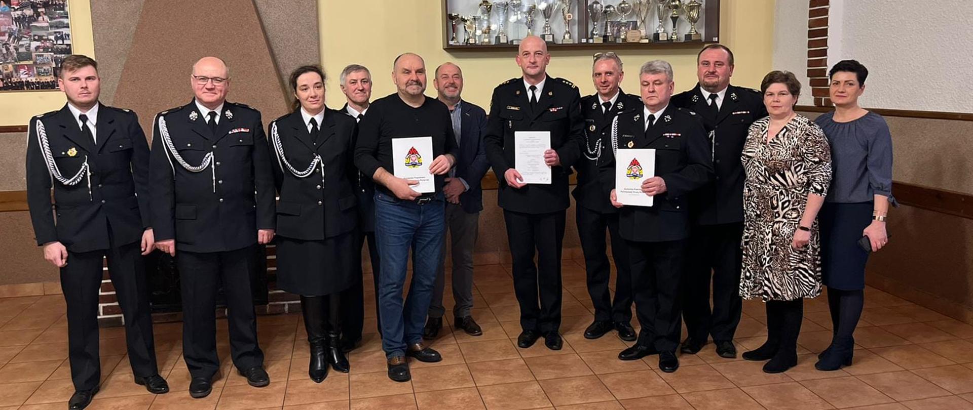 Dwunastu uczestników uroczystego podpisania porozumienia, stoją w szeregu, pozując do zdjęcia i prezentując podpisane dokumenty.