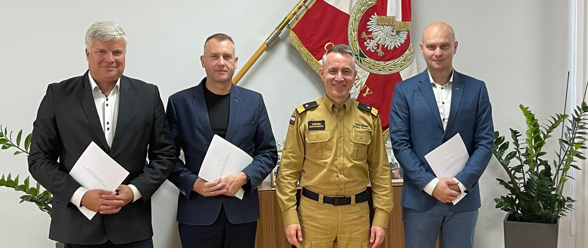 Komendant główny wraz z przewodniczącymi central związkowych pozujący do zdjęcia pamiątkowego. W tle sztandar Komendy Głównej Państwowej Straży Pożarnej 