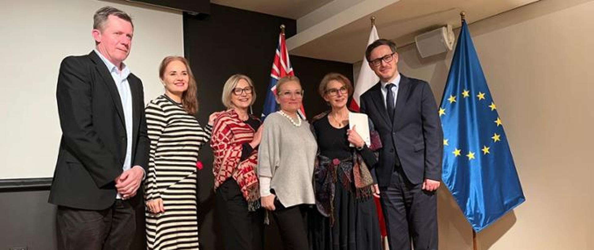Five participants in the event pose against a backdrop of the Polish, European Union, and Australian flags
