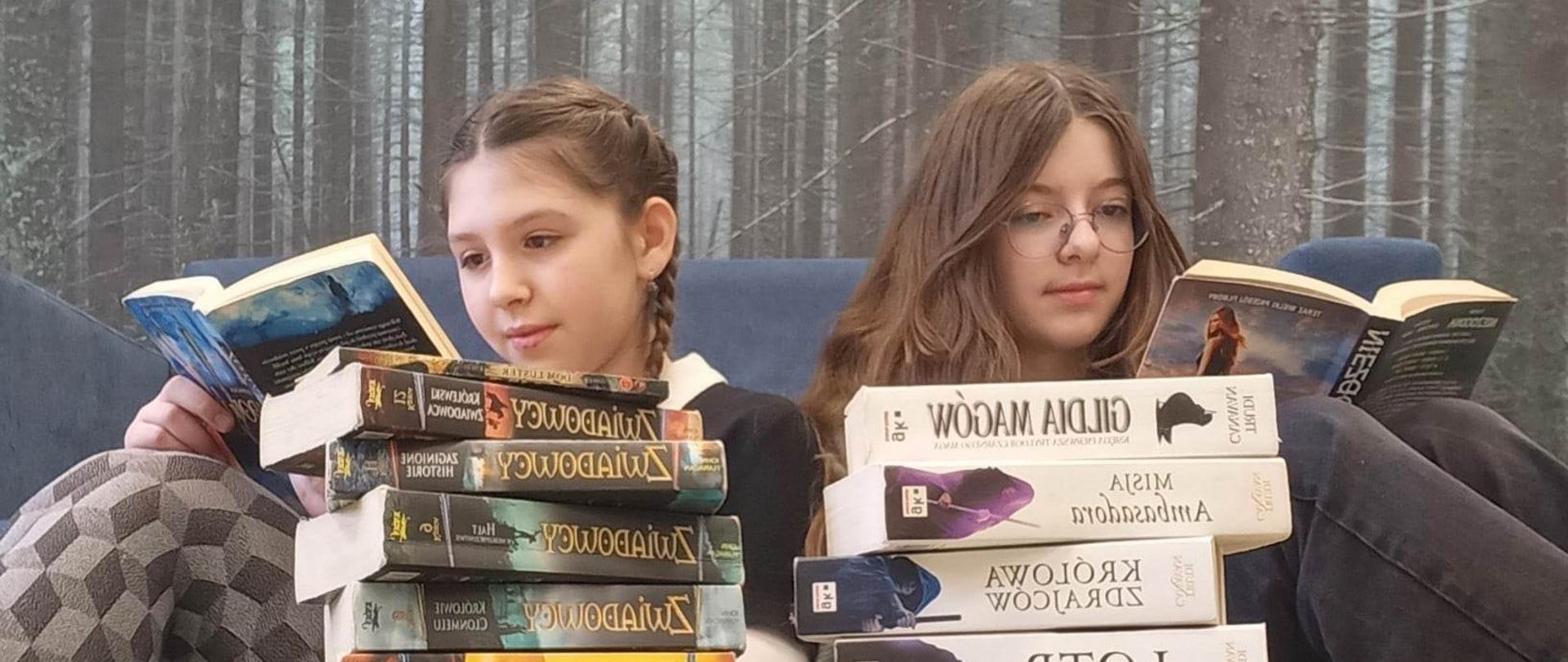 na tle lasu dwie postacie dziewcząt czytających książki, przed nimi ułożone stosy książek