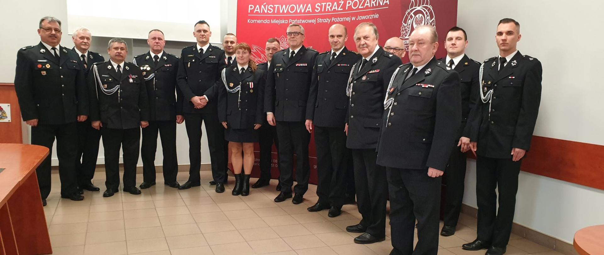 Zdjęcie przedstawia strażaków w mundurach galowych stojących na sali sztabowej w budynku KM PSP w Jaworznie