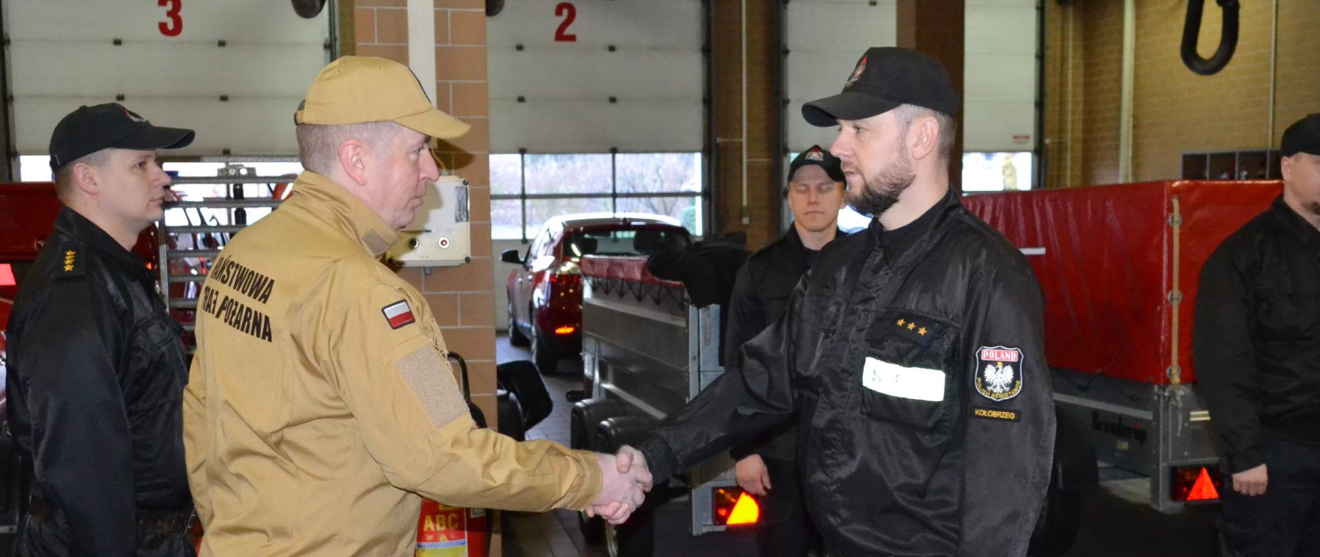 Komendant gratulujący awansu, w tle pojazdy strażackie