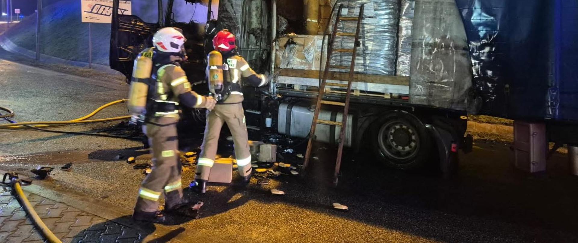 Na zdjęciu znajduje się ciągnik siodłowy z naczepą oraz strażacy w nomexach i sprzęcie OUO