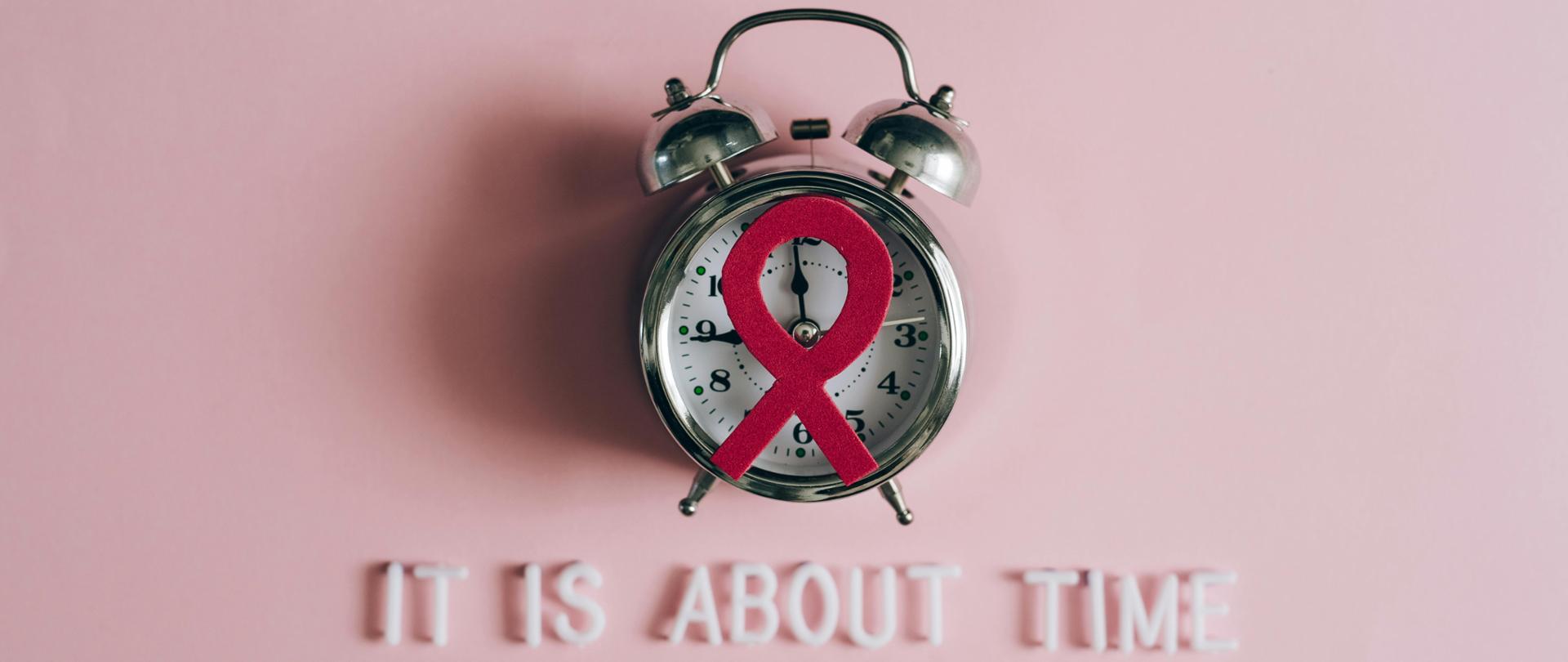 Zdjęcie przedstawiające budzik z wstążeczką symbolizującą AIDS oraz napis It is about Time