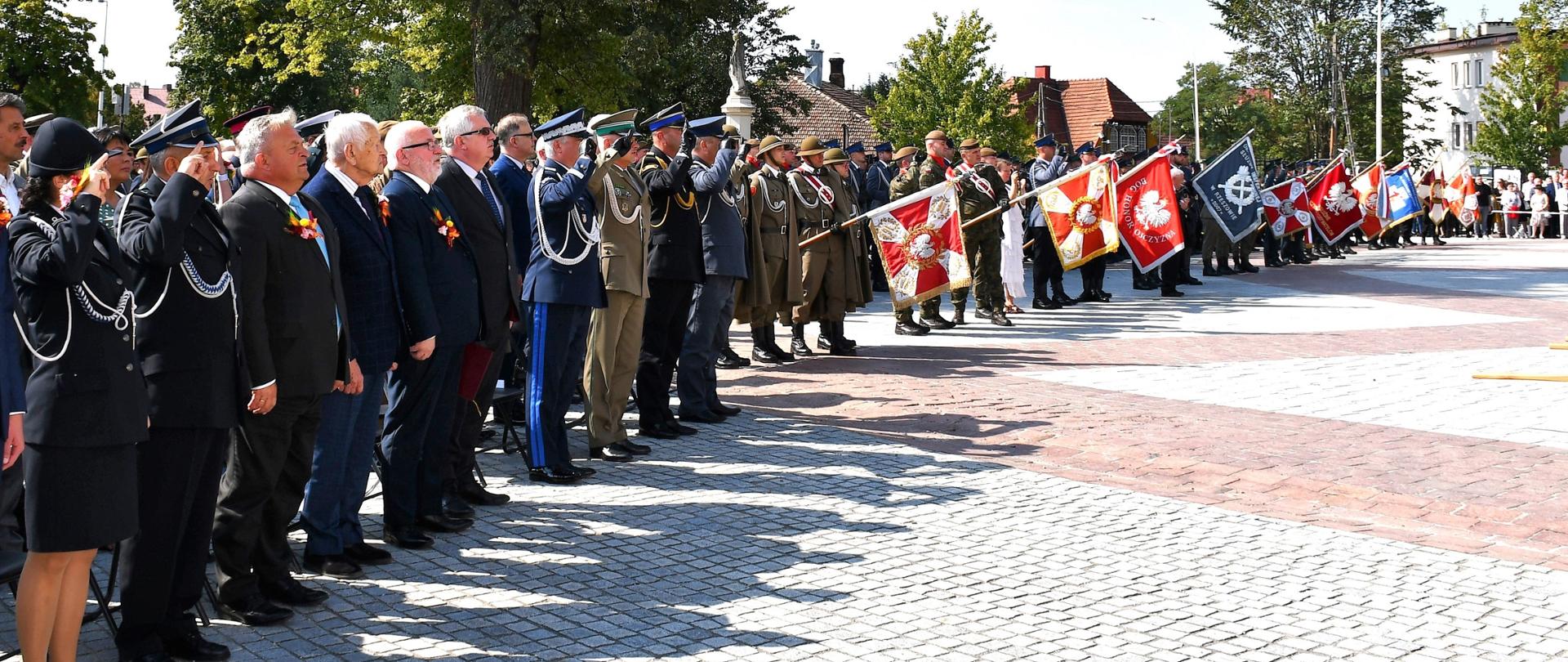 Na zdjęciu widzimy zgromadzone na placu służby mundurowe oraz władze państwowe oddające honory podczas Hymnu Państwowego.