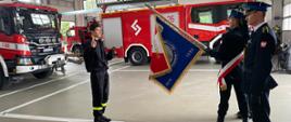 Ślubujący strażak na tle pojazdów strażackich, przed nim sztandar komendy