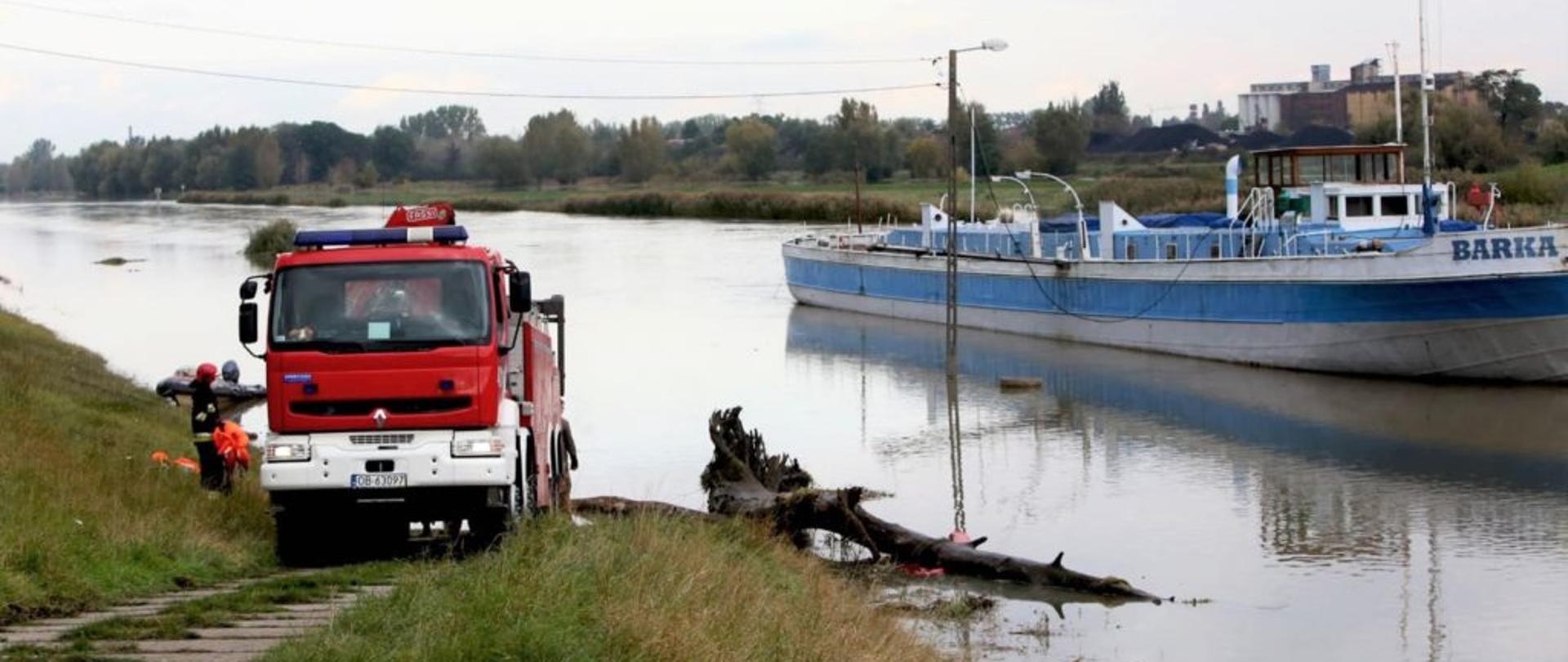 Zdjęcie przedstawia samochód SCRt "Mega City" podczas usuwania konaru drzewa zalegającego na Kanale Ulgi w Opolu. W tle widoczna jest barka o którą zaczepiły się konary drzewa.