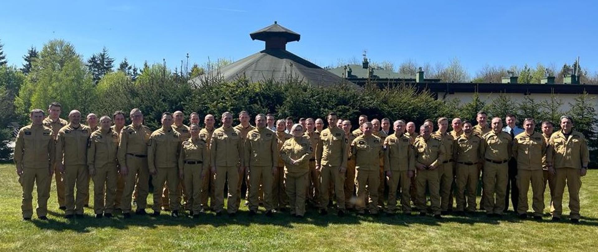 Grupowe zdjęcie uczestników narady na otwartym zielonym terenie. Wszyscy ubrani są w mundury służbowe koloru piaskowego