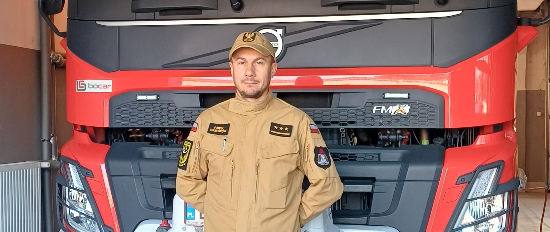 kpt. Paweł Grześków pozujący do zdjęcia na tle samochodu pożarniczego