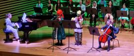 Dzieci przebrane w stroje z filmu "Shrek" grają na wiolonczeli, fortepianie i dwoje na skrzypcach.