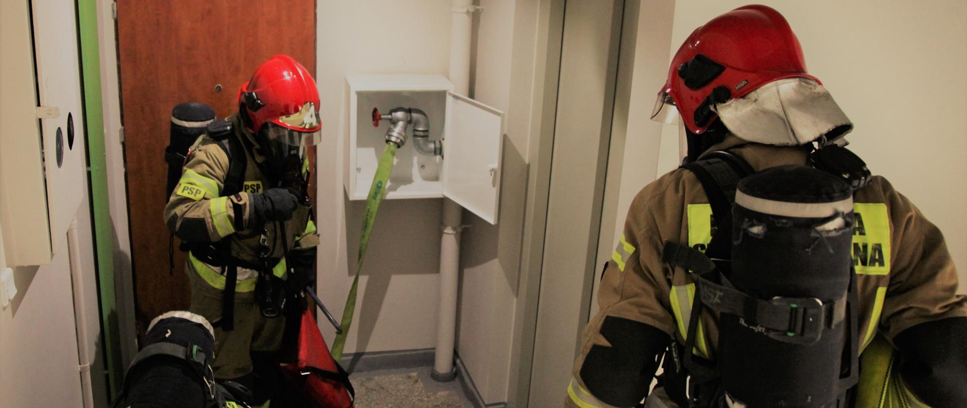 Trzech strażaków ubranych w aparatach ochrony układu oddechowego na klatce schodowej 