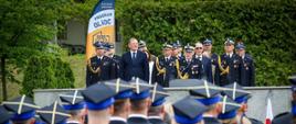 Do mikrofonu przemawia Zastępca Komendanta Głównego PSP nadbryg. Paweł Frysztak. Za nim goście uroczystości. Wśród nich Komendant Miejski PSP m. st. Warszawy st. bryg. Paweł Adamczyk, Mazowiecki Komendant Wojewódzki PSP nadbryg. Artur Gonera oraz Rektor-Komendant Akademii Pożarniczej nadbryg. Tomasz Klimczak. 