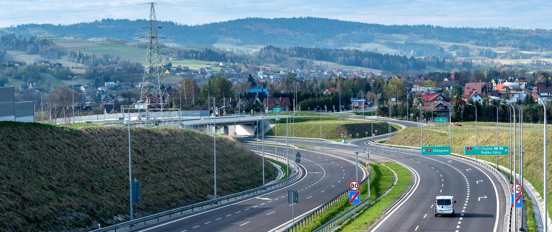 droga dwujezdniowa i węzeł drogowy w górskim terenie, w tle zabudowania i pasmo górskie