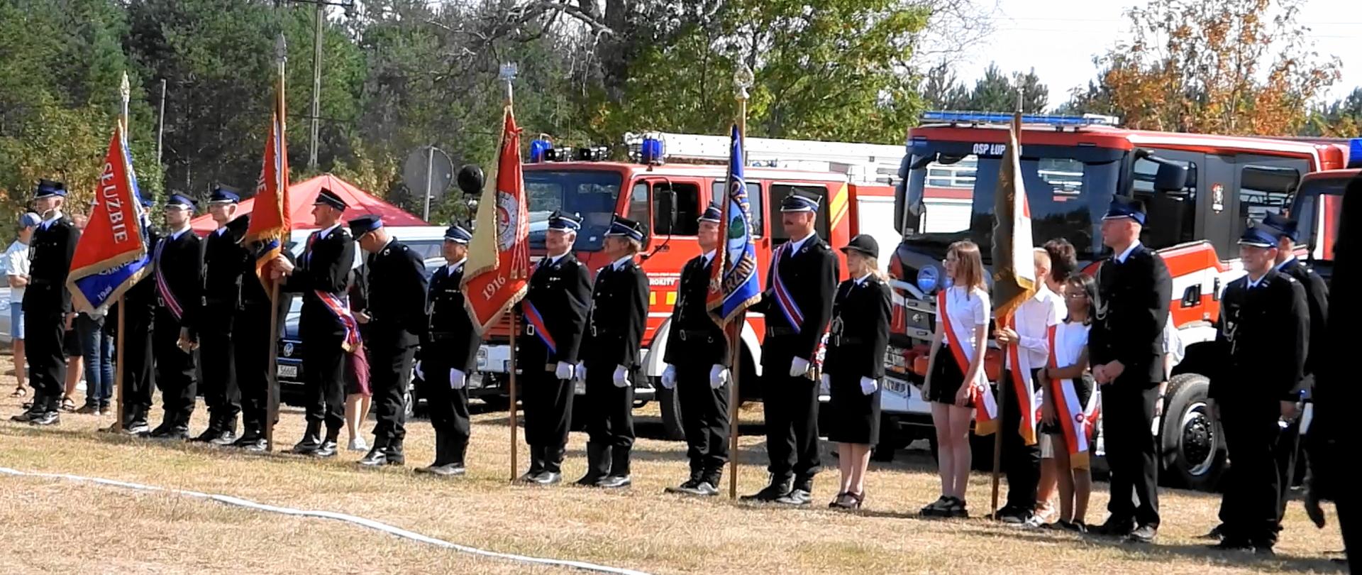 W rzędzie przy wozach strażackich stoją przedstawiciele pięciu pocztów sztandarowych