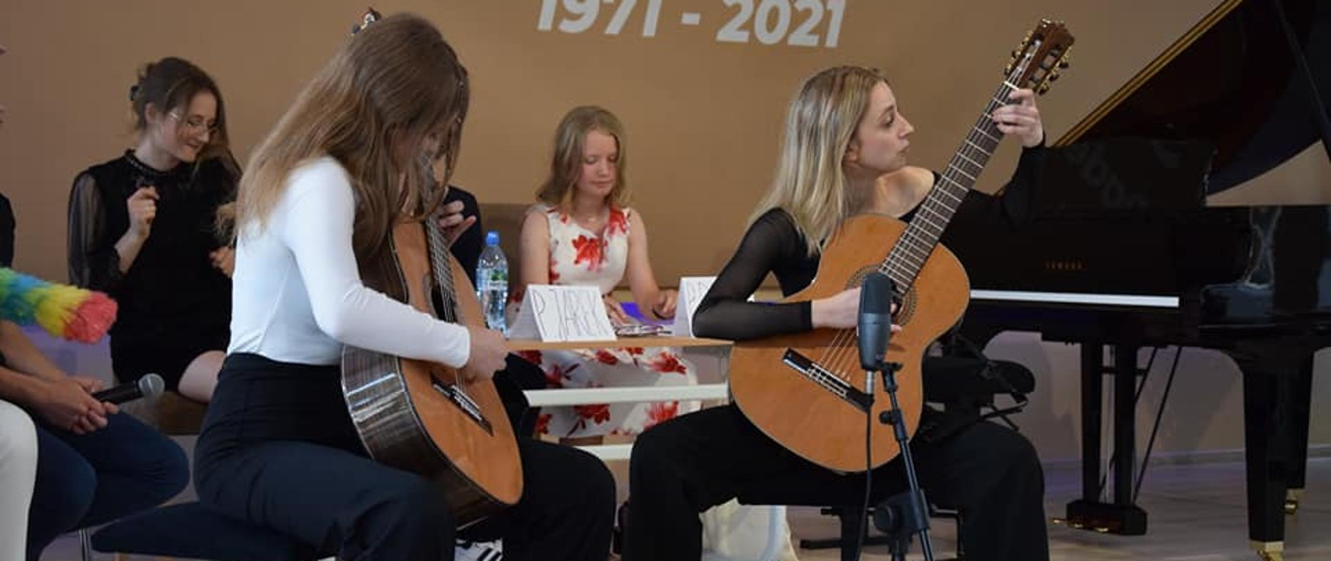 na scenie gra duet gitarowy, na drugim planie siedzą uczniowie