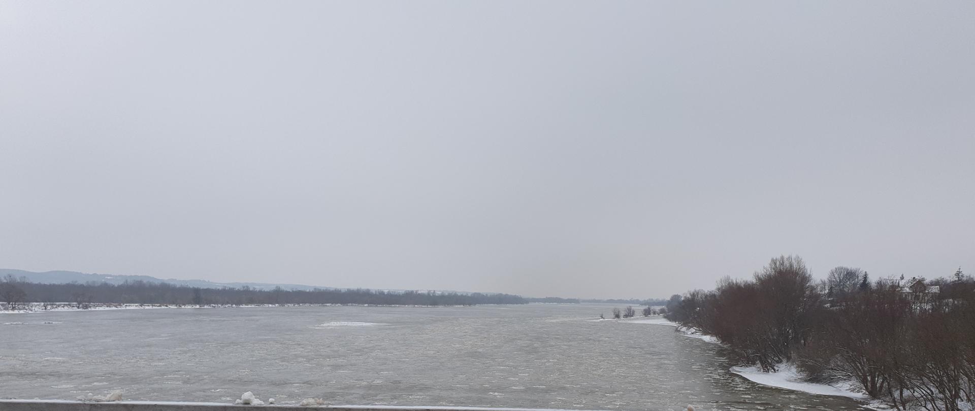 Zdjęcie przedstawia rzekę Wisła. Na powierzchni lustra wody znajdują się pojedyncze kry lodowe.