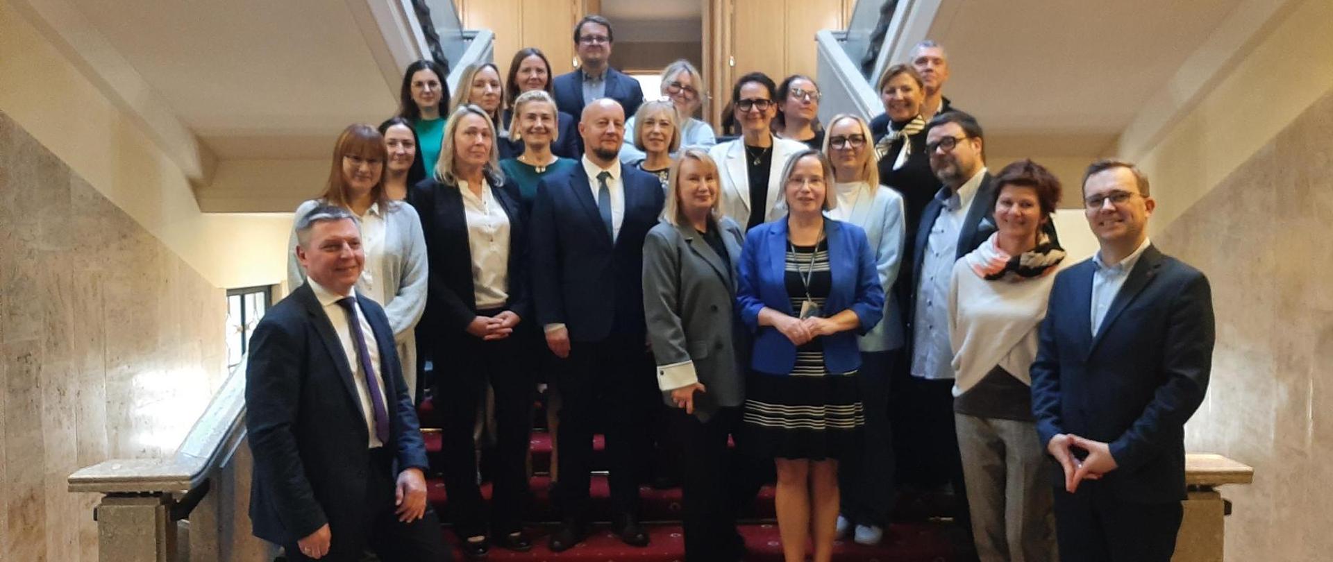 Uczestnicy spotkania grupowego pozują do wspólnego zdjęcia na schodach wewnątrz budynku
